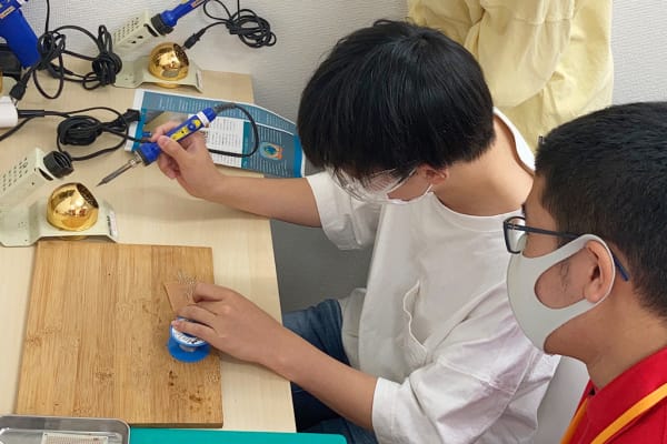 はんだごてを使った部品の接着、火傷をしないように細心の注意を払って指導し、作業を進めます。【2023年6月撮影】