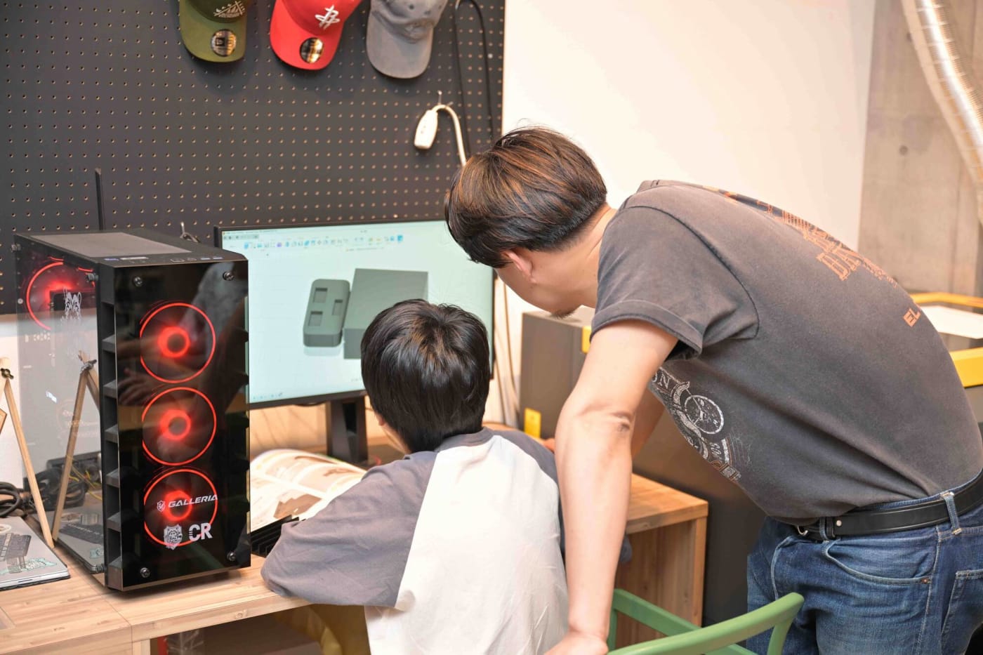 ロボットのデザインを行っている小学生の男の子と後ろからアドバイスする先生