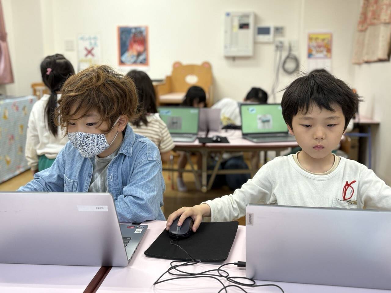 並んでパソコンでプログラミングをする小学生。