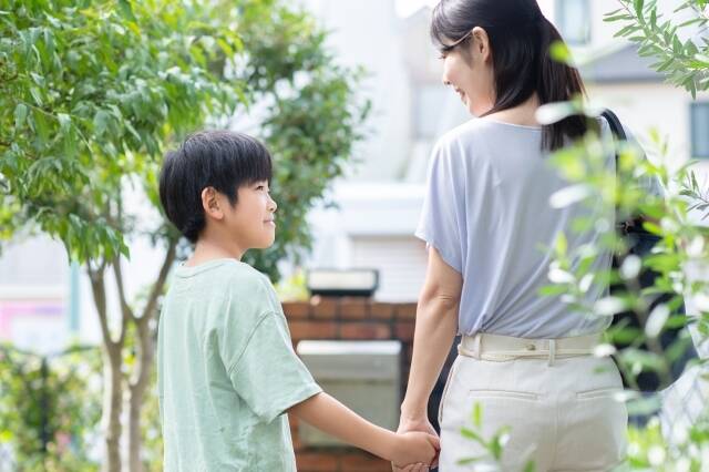 小学生と母親が手をつないで歩きながら話している