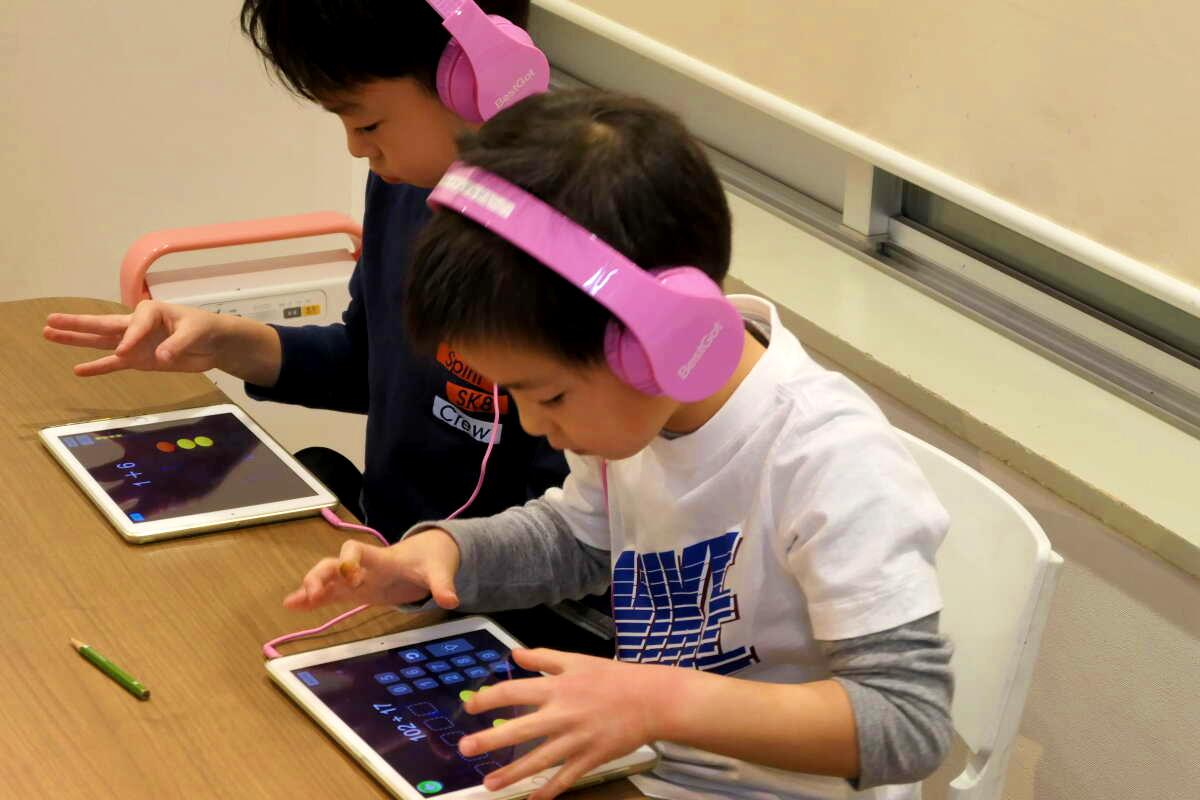 ピンクのヘッドフォンをつけた2人の子供がタブレットを使用しています