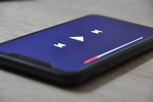 スマートフォンの画面に表示された動画プレーヤーの再生画面。中央に再生ボタン、左右に巻き戻し・早送りボタン、画面下部には再生バーが表示されている。