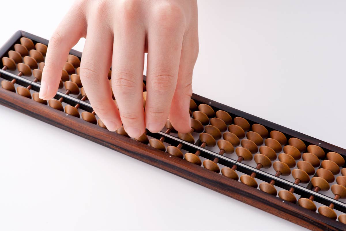 女性の手がそろばんのボタンを押しています