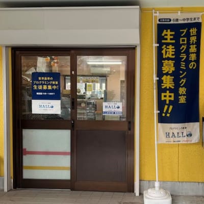 入口のポスターと、HALLOのノボリが目印です。入口は鍵がかかっていることが多いので、インターホンにてお知らせください。