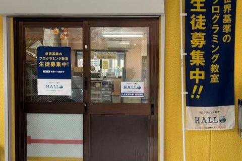 入口のポスターと、HALLOのノボリが目印です。入口は鍵がかかっていることが多いので、インターホンにてお知らせください。