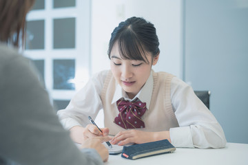 生徒が学習している様子を捉えた画像であり、机の上にはノートやペンが置かれている。生徒は制服を着ており、集中している様子が見受けられる。