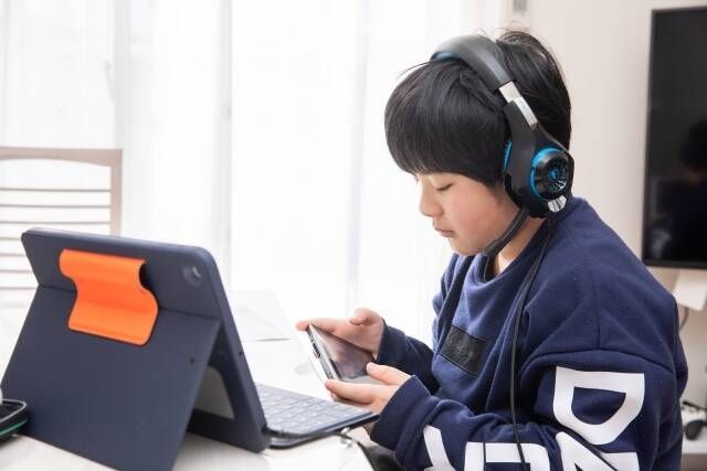 タブレットにスマホも見ている小学生の男の子の姿