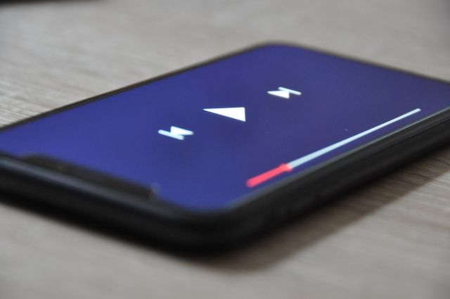 スマートフォンの画面に表示された動画プレーヤーの再生画面。中央に再生ボタン、左右に巻き戻し・早送りボタン、画面下部には再生バーが表示されている。