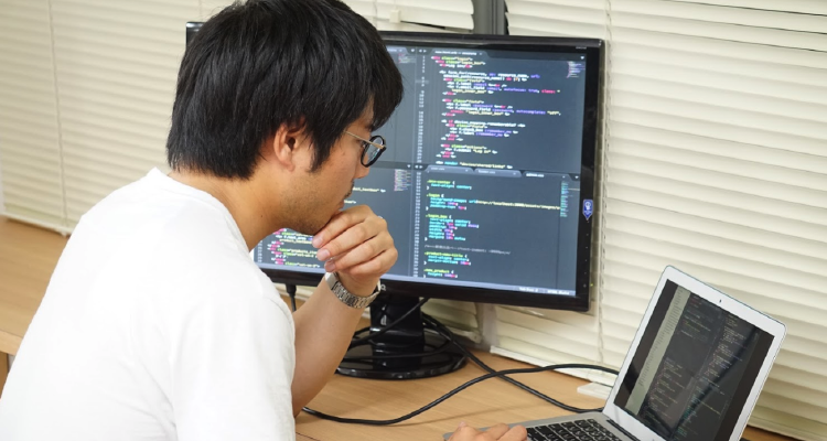 男性がモニターとPCを見ながらプログラミング学習をしている