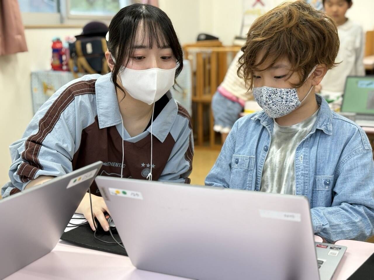 パソコンでプログラミングをする男の子を指導する先生。