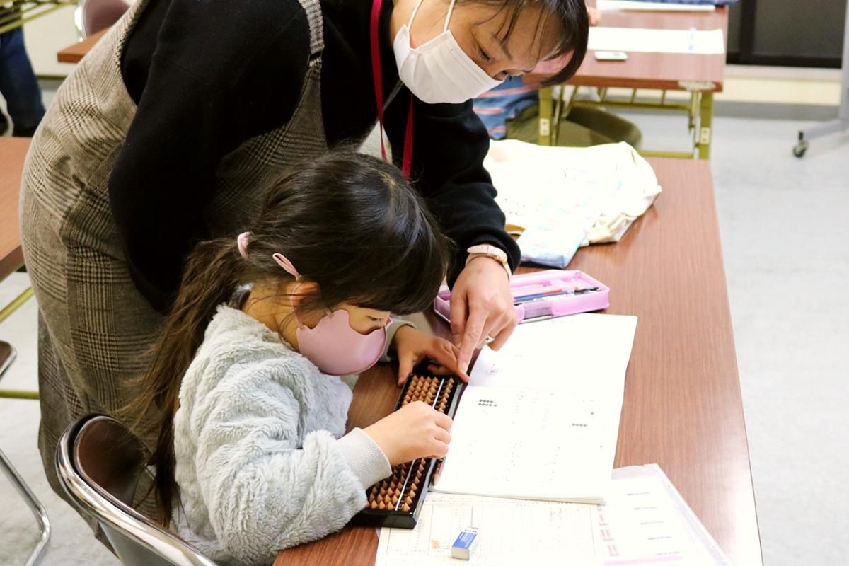 算盤を使用している女の子と隣に立っている女性