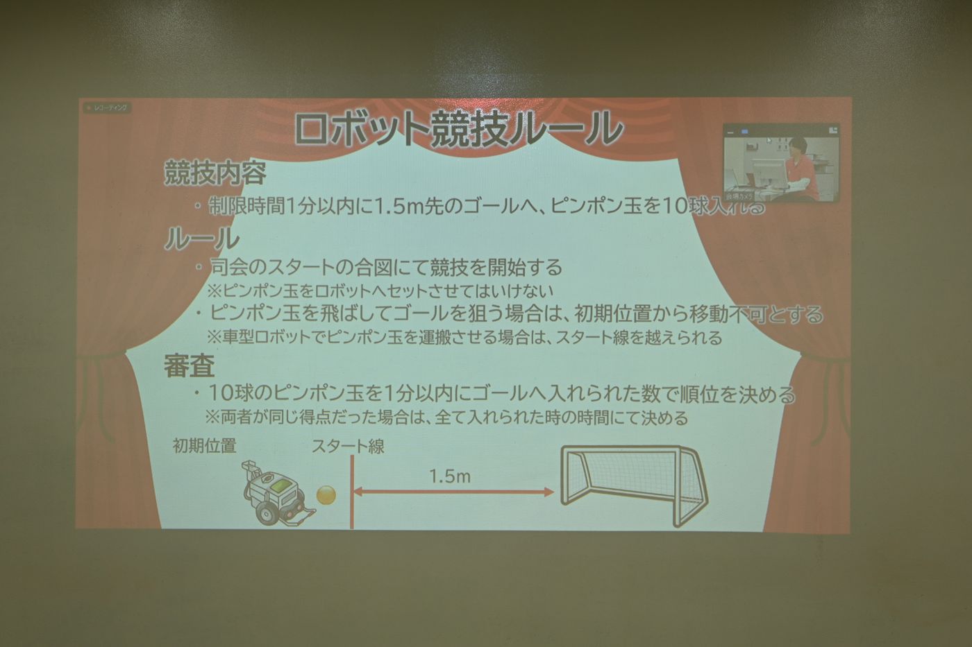 ロボット競技のルールを説明するスライド。競技内容は、制限時間1分以内に1.5m先のゴールへピンポン玉10球を入れること。ルールや審査基準、開始位置、ゴールとの距離などが視覚的に詳しく解説されている。