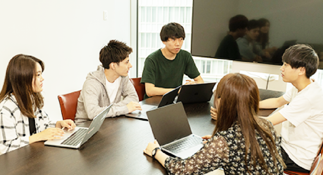 会議室の机に6名の生徒が集まって座っている。それぞれPCを持っており、何かを議論している