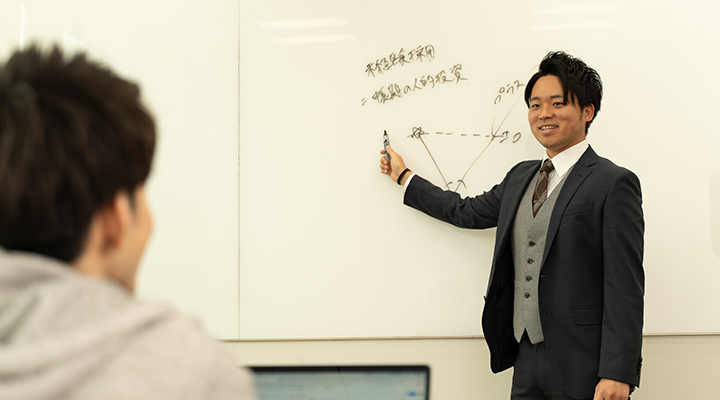 先生がホワイドボードに何かを書いて生徒に教えている