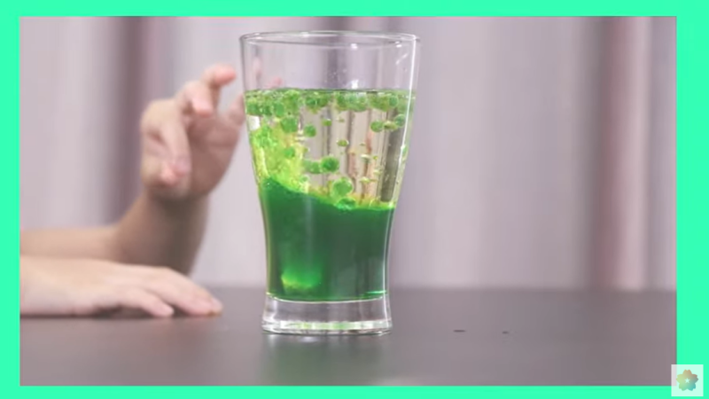 緑色の液体が入ったグラスを持っている人。