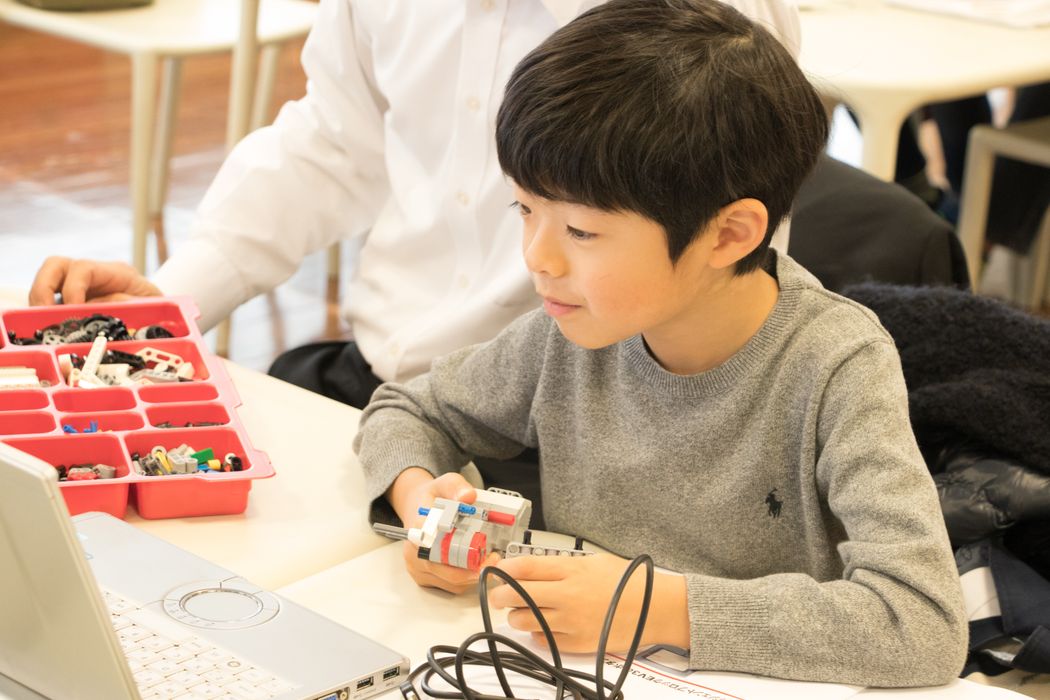 グレーのセーターを着た少年がノートパソコンの前に座っている