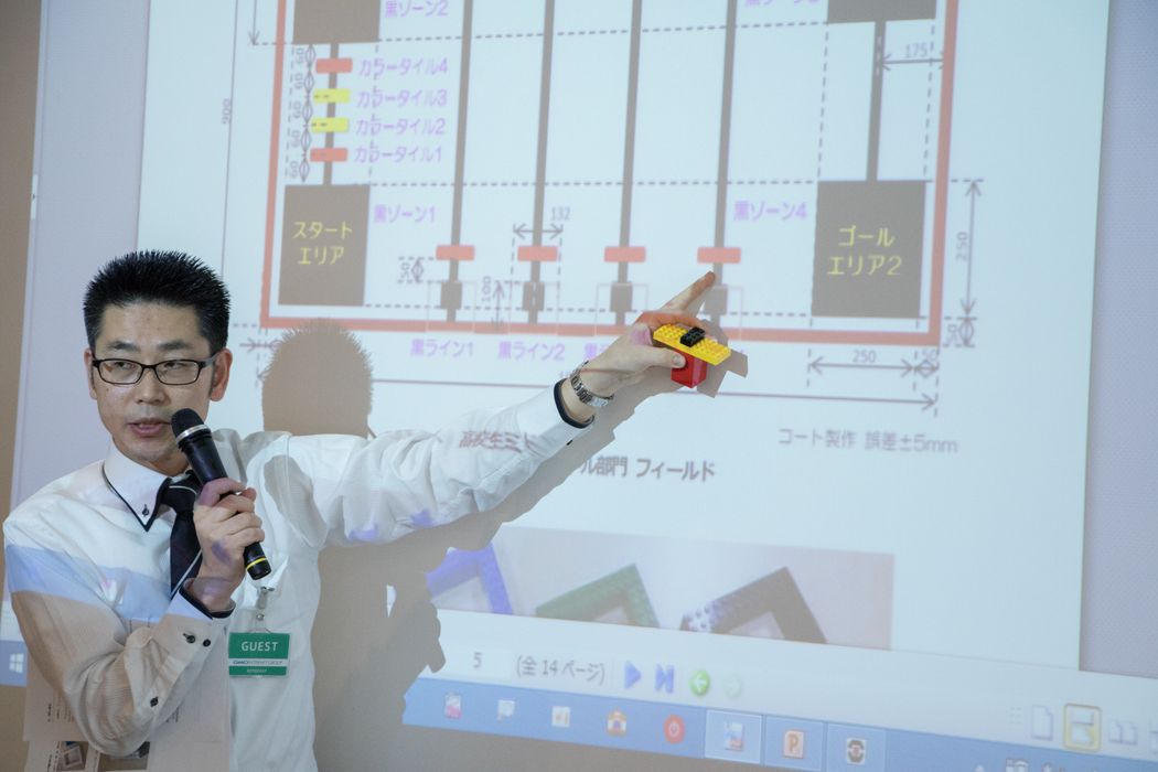 男性がマイクを持ってプレゼンテーションをしている