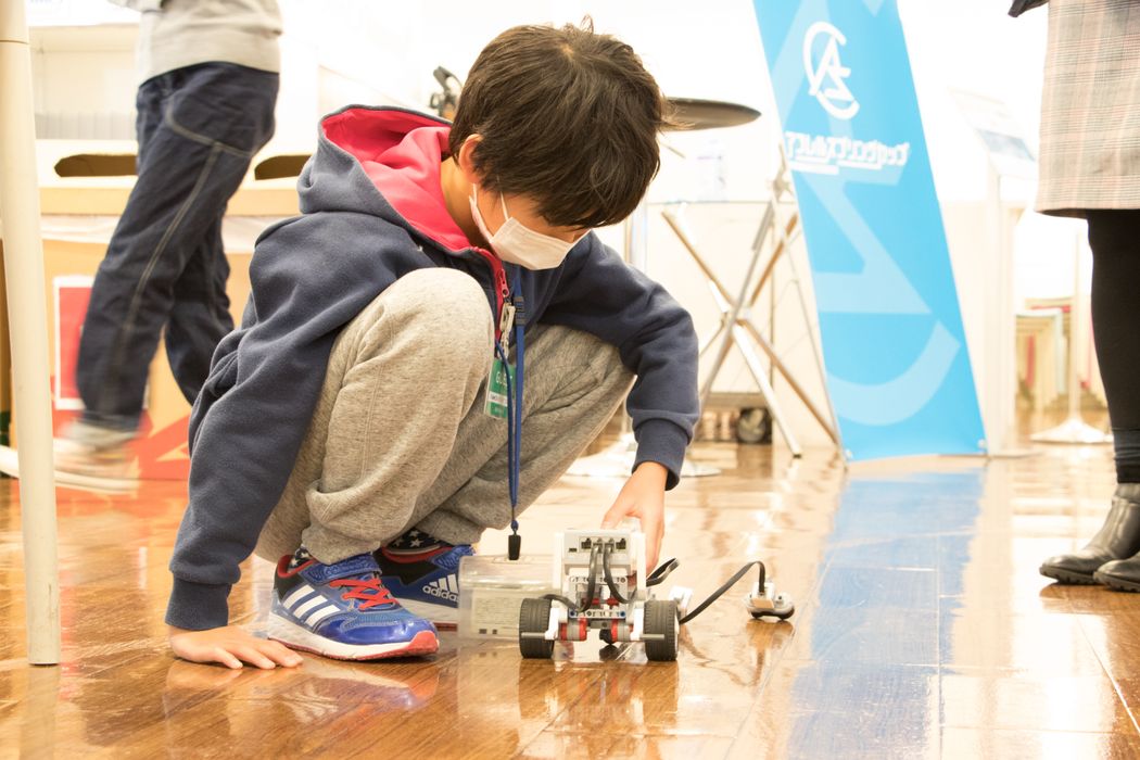 白いマスクをかけた少年がおもちゃの車を運転しています